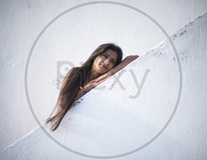 An young and attractive Indian brunette woman in red western dress standing on the stair case on the rooftop in a morning. Indian lifestyle and quarantine.