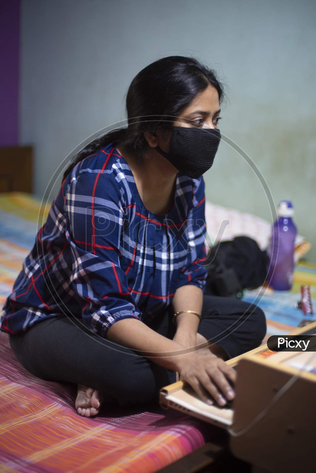 Portrait of an Indian young woman with Corona preventive mask sitting at home with a computer in  home isolation due to covid - 19. Indian lifestyle and disease.