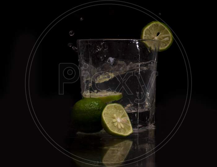 Water splashes out of the garnished glass as a green fresh lemon slice immerses into the water.