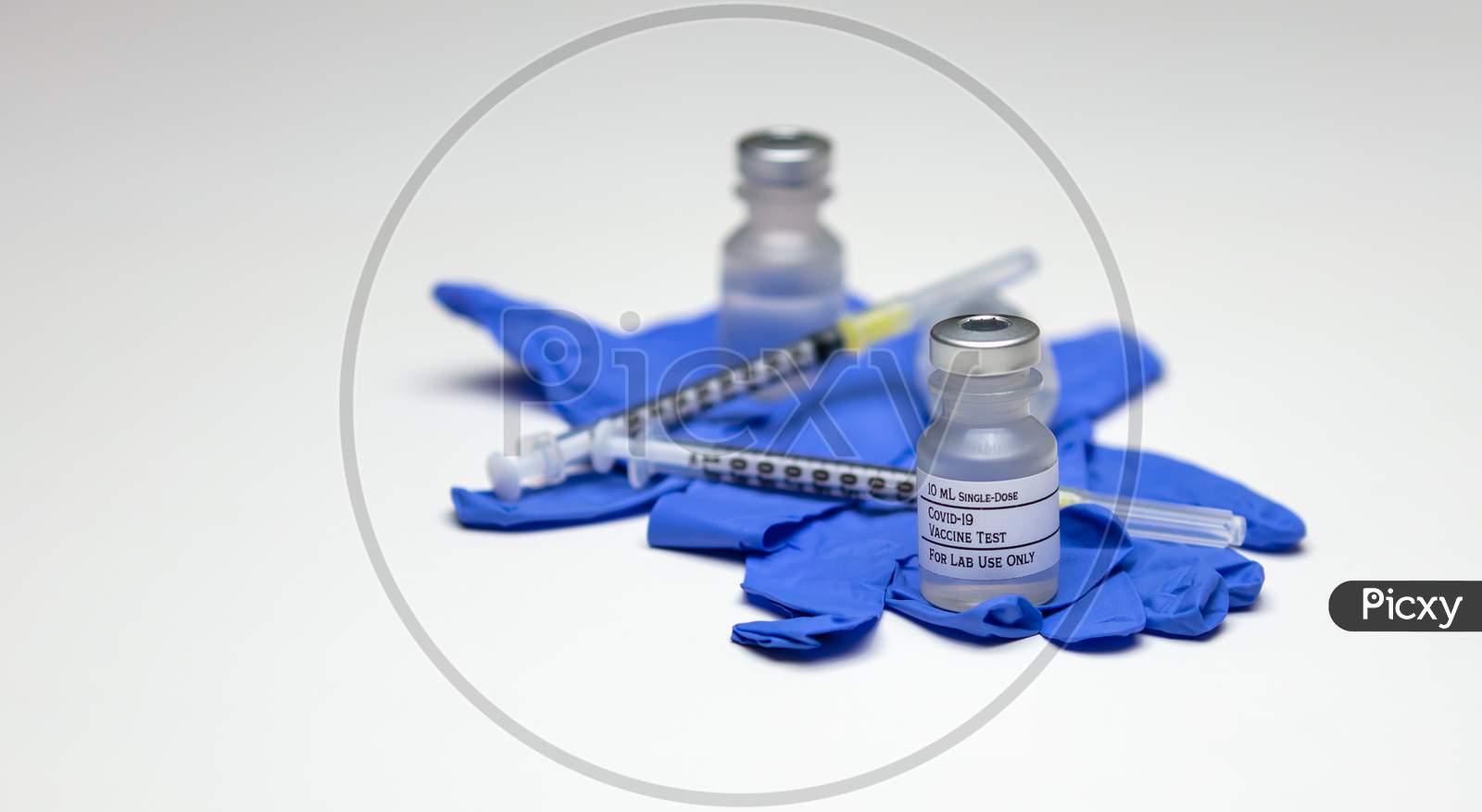 A Pair Of Covid-19 Test Vaccine Vials On Top Of Blue Rubber Medical Gloves With Syringes.