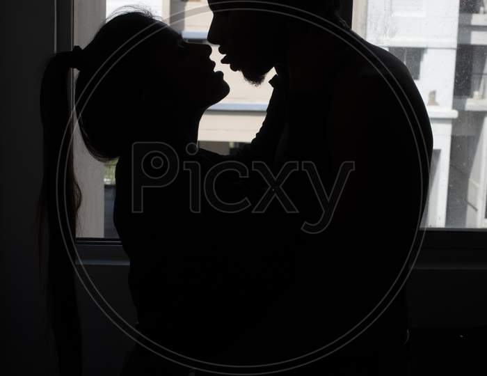 Silhouette of an Indian romantic couple kissing in front of a window. Intimate couple lifestyle