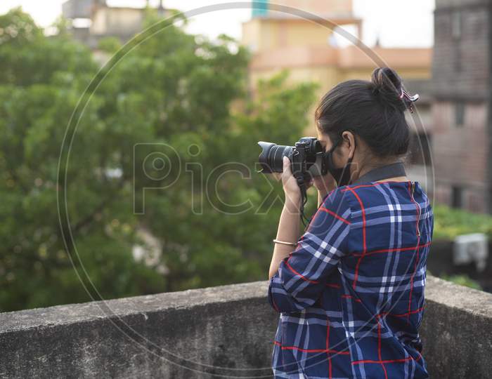 Portrait of an Indian young woman with corona preventive mask taking photograph in back light on a rooftop in home isolation.Indian lifestyle, disease and home quarantine.