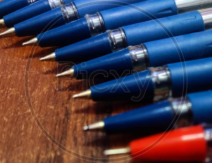 Stockpiled blue and red ball pin point pens lying on a wooden table vertical image with wooden background