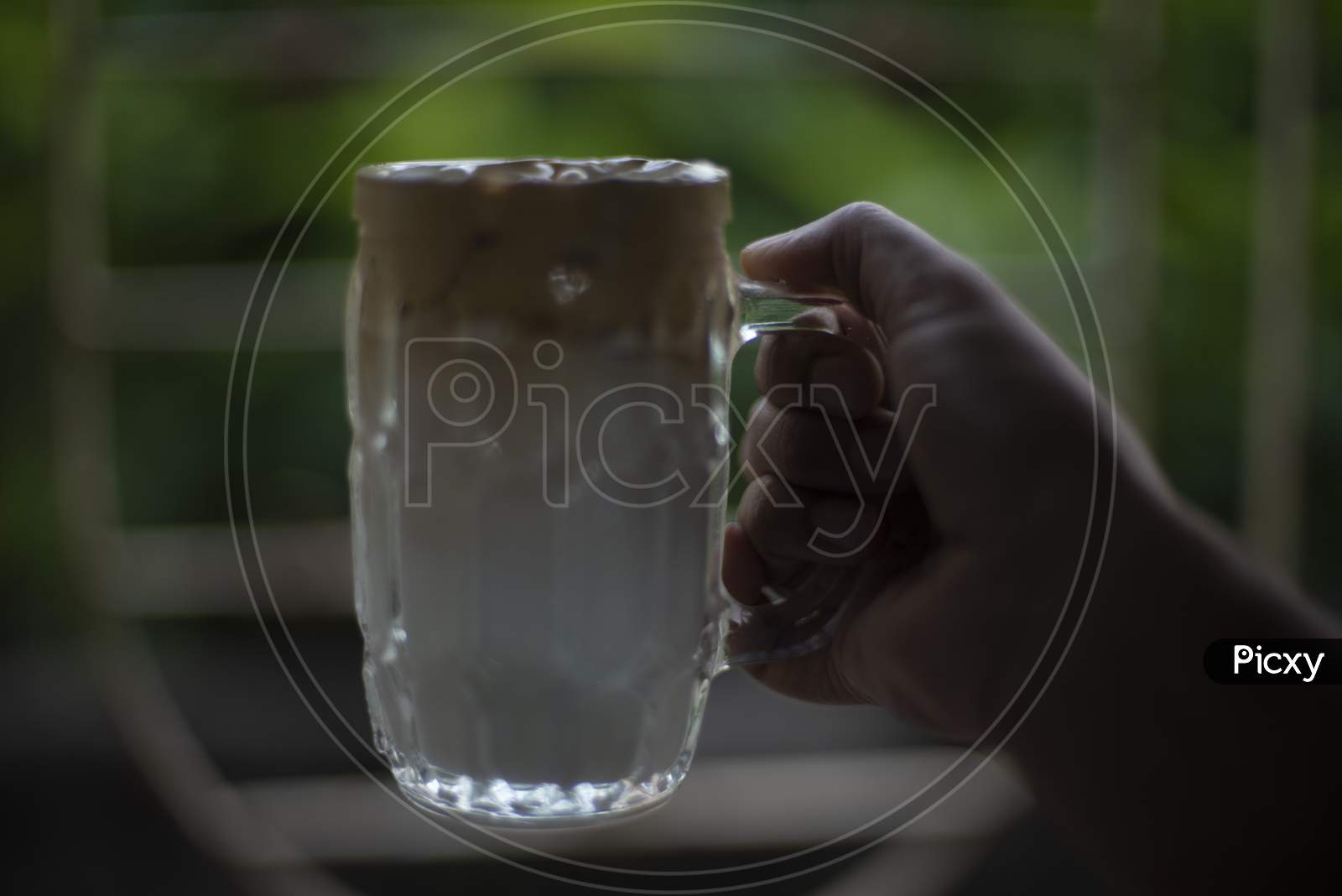 A hand holding a glass of Dalgona coffee  in front of a window. Refreshment and drink