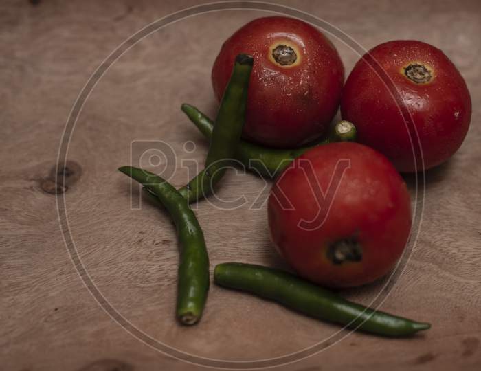 Top view of fresh red tomatoes and green chilies are kept on a wooden tray in a dark copy space background.