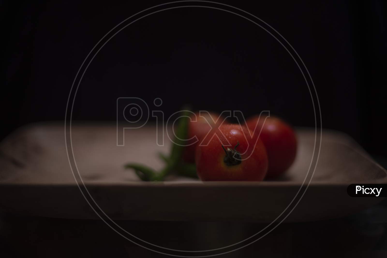 Fresh red tomatoes and green chilies are kept on a wooden tray in a dark copy space background