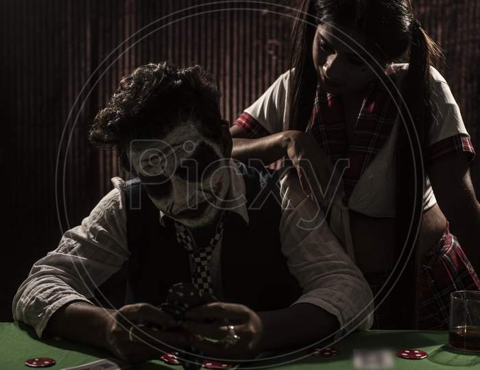 Portrait of an Indian couple in Halloween Joker costume playing cards in a casino poker table in textured studio background. Cosplay photography.