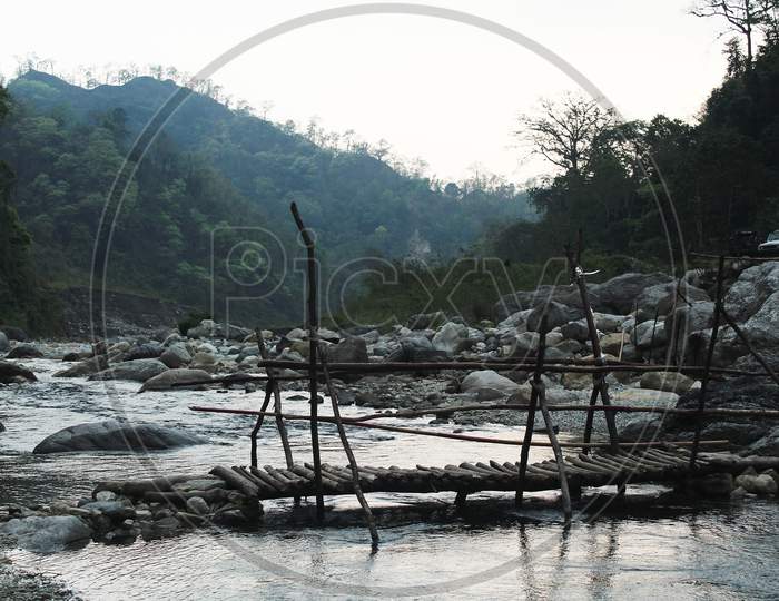 Scenario Of Little River And A Foot Bridge Beside A Range Of Mountains