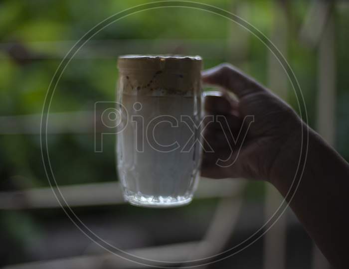 A hand holding a glass of Dalgona coffee  in front of a window. Refreshment and drink