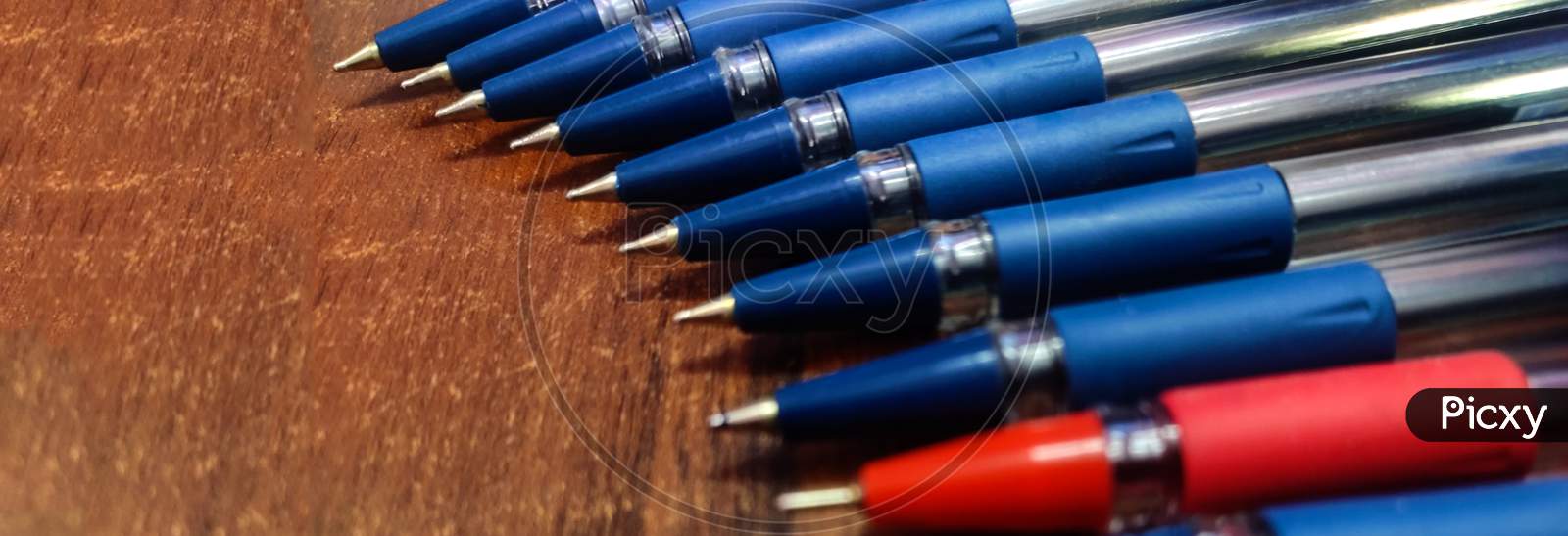 Stockpiled blue and red ball pin point pens lying on a wooden table vertical image with wooden background