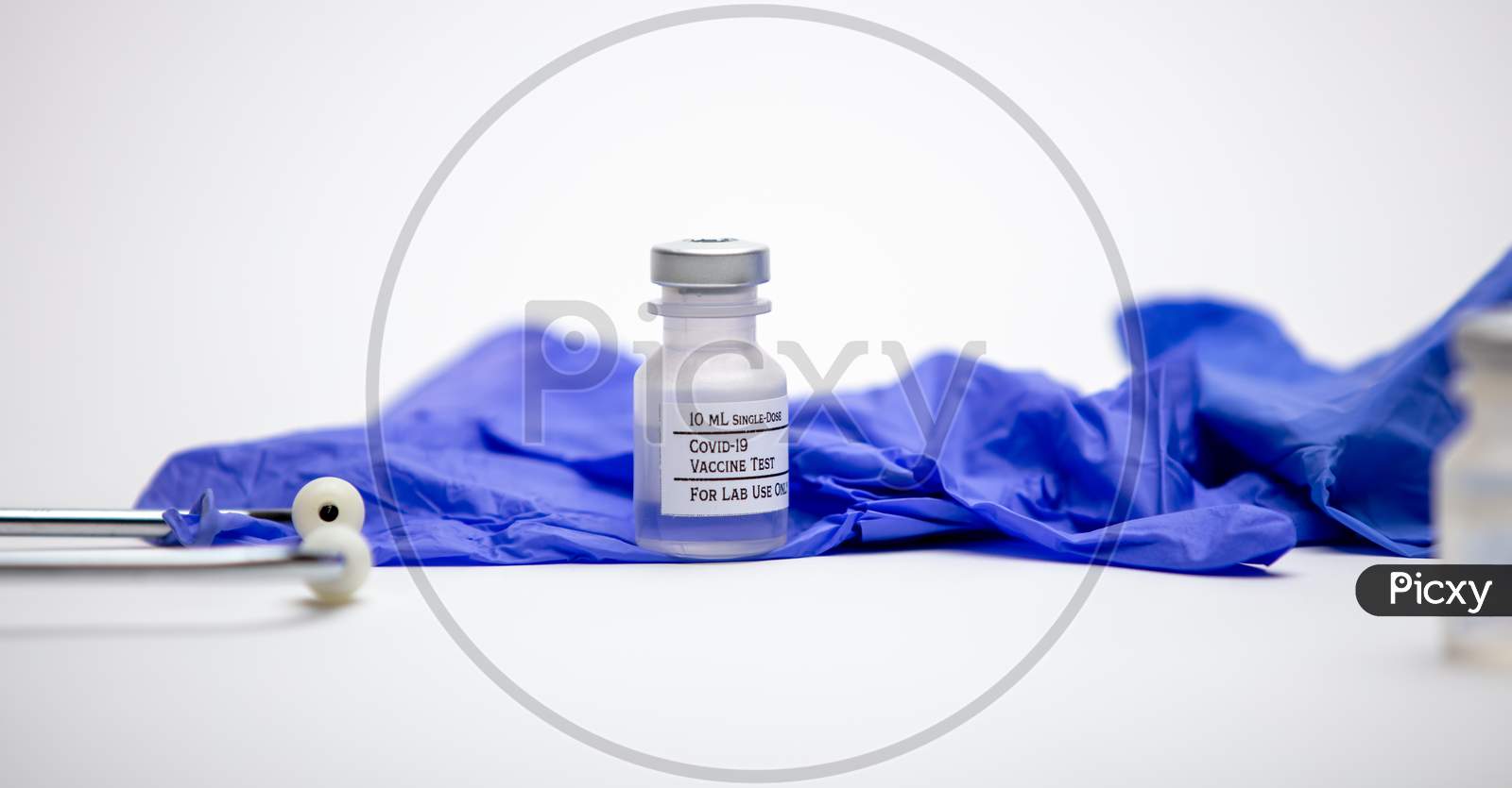 A Vial Of Covid-19 Test Vaccine Sits On Top Of Blue Rubber Medical Gloves. Stethoscope On Side.
