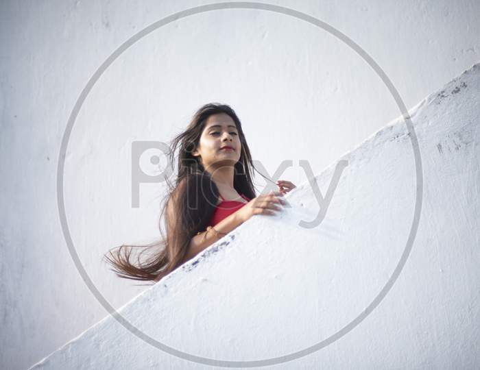An young and attractive Indian brunette woman in red western dress standing on the stair case on the rooftop in a morning. Indian lifestyle and quarantine.