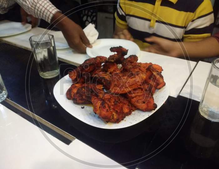 Chicken tandoori served on white plate, A mughal dish, people hands on plate sharing food with others,