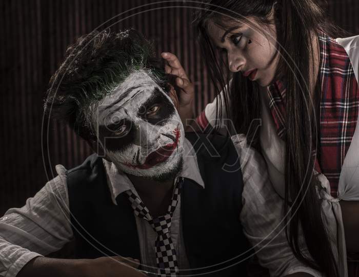Portrait of an Indian couple in Halloween Joker costume playing cards in a casino poker table in textured studio background. Cosplay photography.