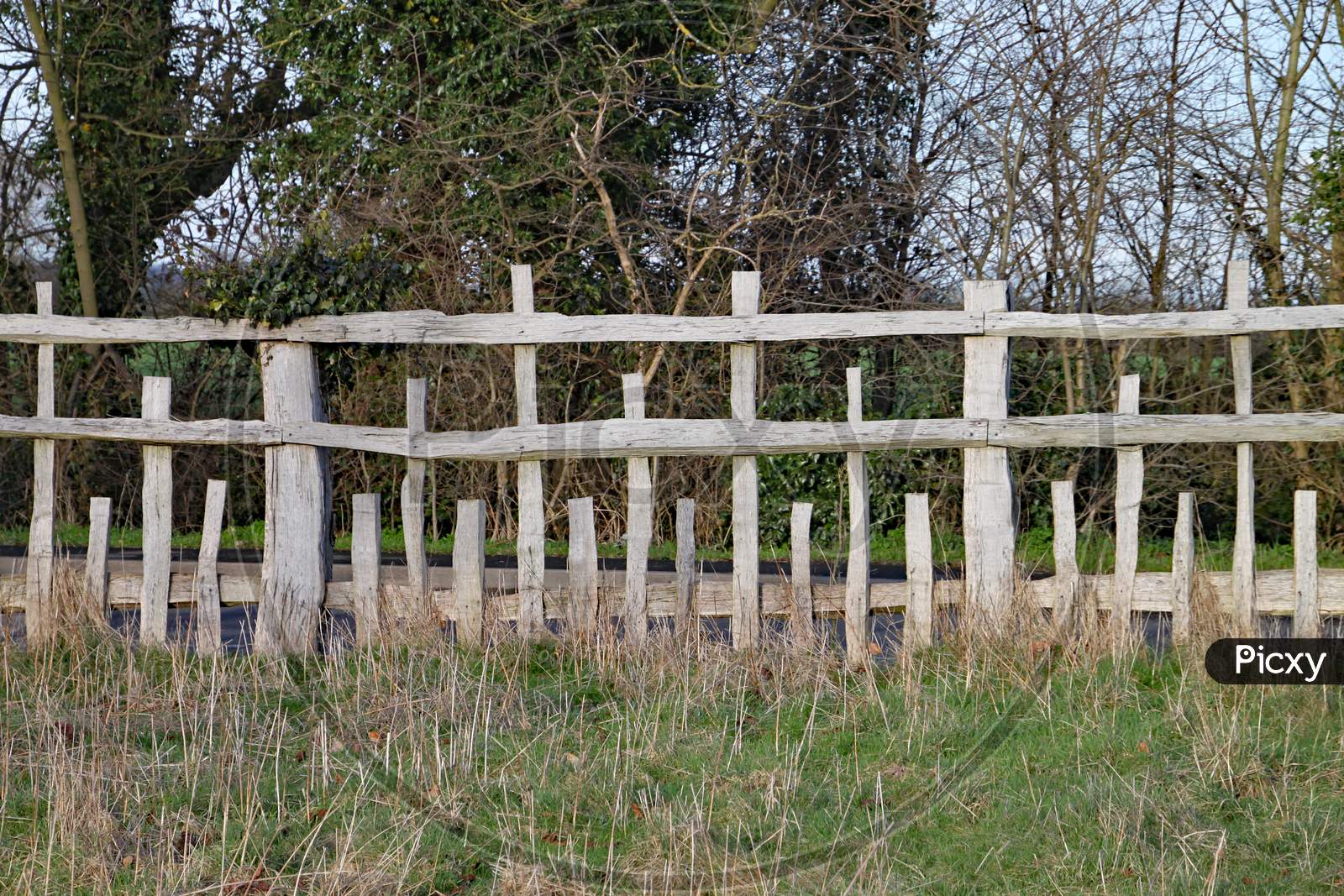 Unusual Wooden Fence With Parallel Horizontal Rails And Vertical Posts Of Different Lengths In A Pattern