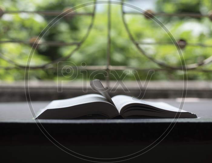 A book is kept open in front of a window with a page mark in a green background.