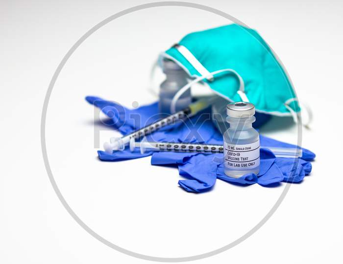 Two Syringes On Top Of Blue Medical Gloves With Two Vials Of Covid-19 Test Vaccine And A Respirator Mask.