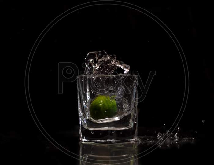 Water splashing out from a glass due to the immersion of a fresh green small lime into it.