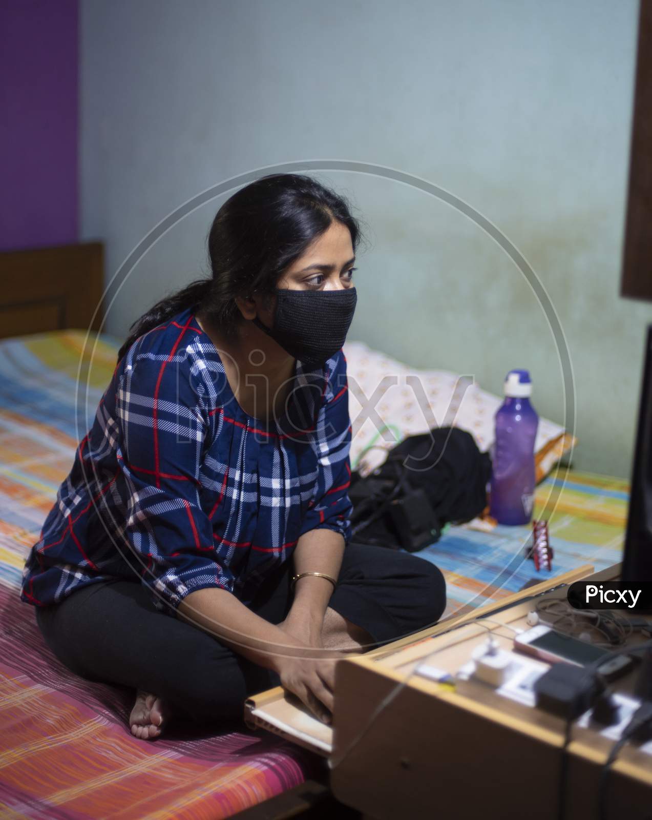 Portrait of an Indian young woman with Corona preventive mask sitting at home with a computer in  home isolation due to covid - 19. Indian lifestyle and disease.
