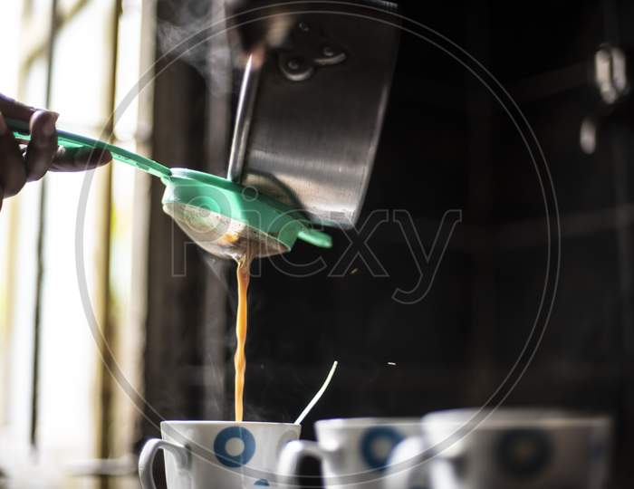Tea being strained and poured into the cups from an aluminium tea pot in an Indian kitchen. Indian drink and beverages.