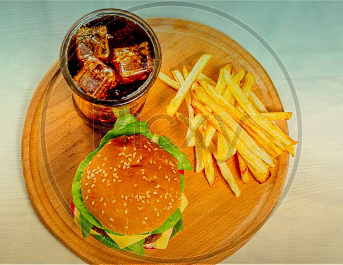 Burger, fries and iced drink on a round wooden plate