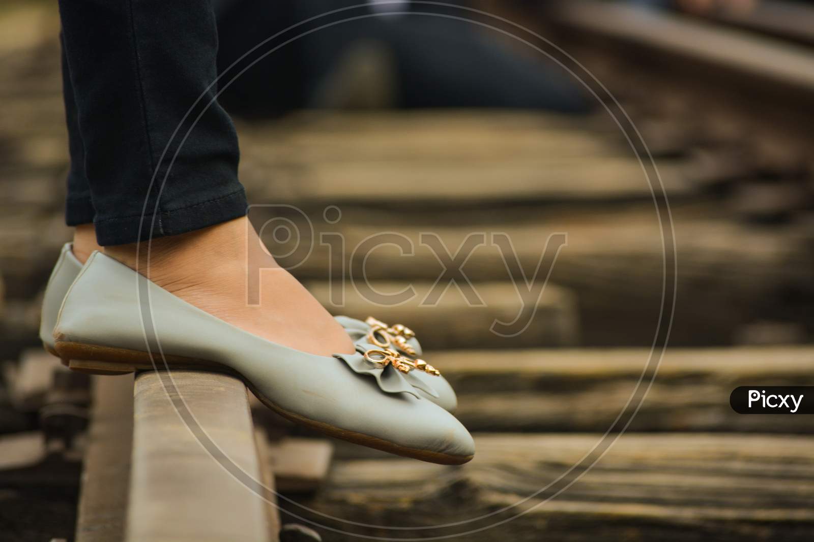 Foot (Feets) Of A Girls Standing On A Railway Track Wearing Grey Coloured Bellies With A Golden Flower On It. Old Fashioned Railway Tracks.