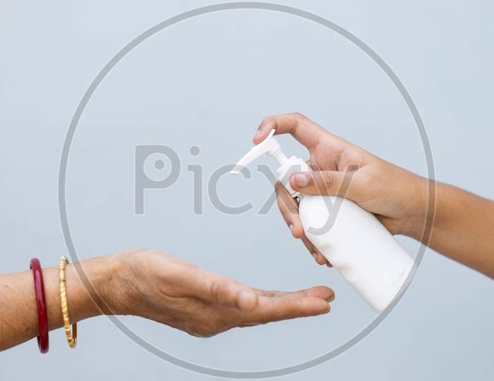 Close Up Of Child And Senior Woman Hand Using Hand Sanitizer Against Plain Background
