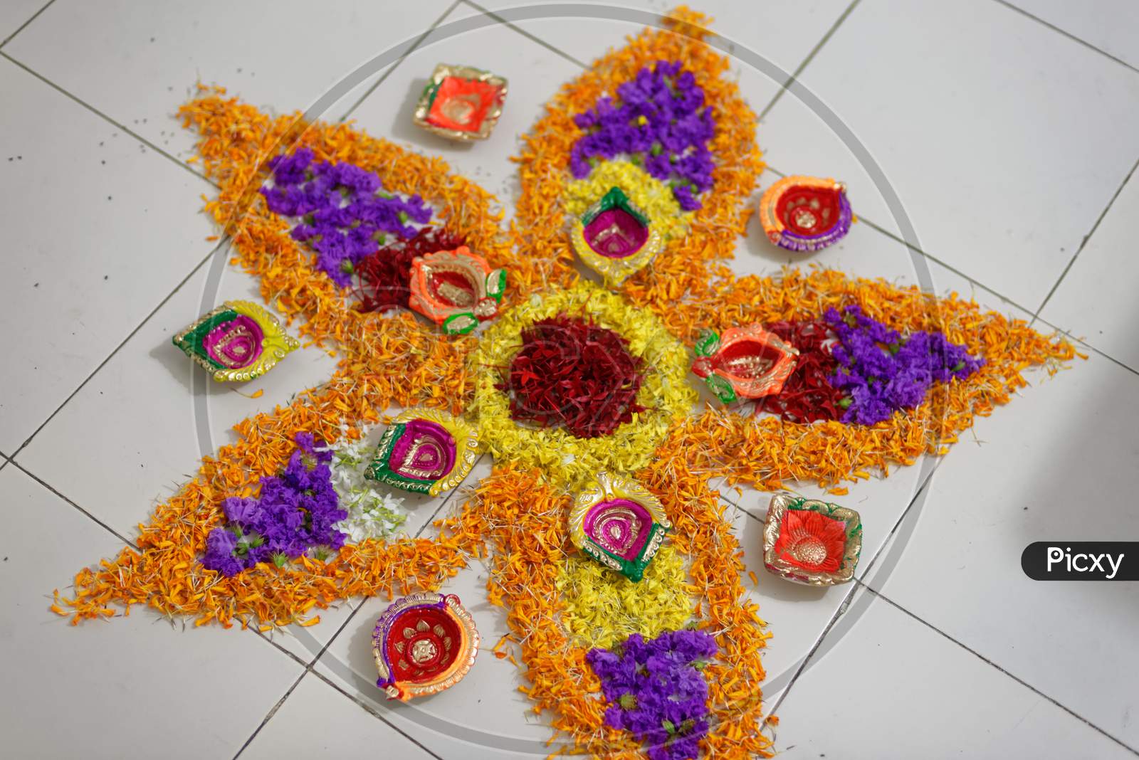 Beautiful holy rangoli is prepared by vibrant colorful flowers and decorative colorful diyas/lamps in white floor. Indian lifestyle and Diwali celebration.