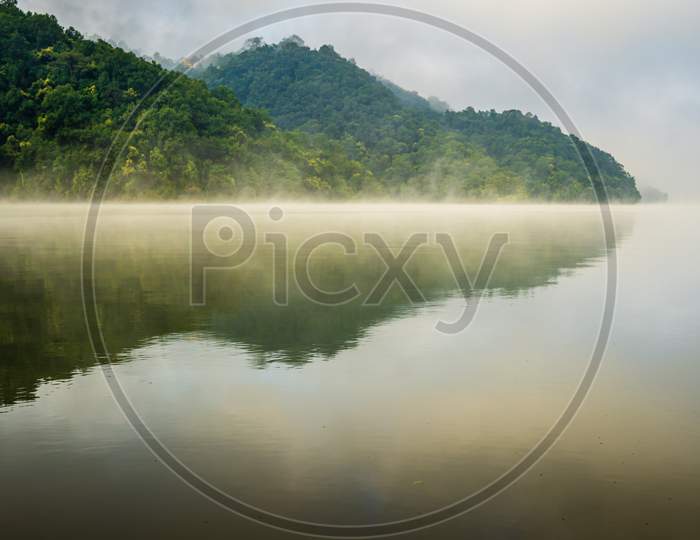 Reflections of hills and forests on foggy surface of Begnas Lake in Pokhara, Nepal