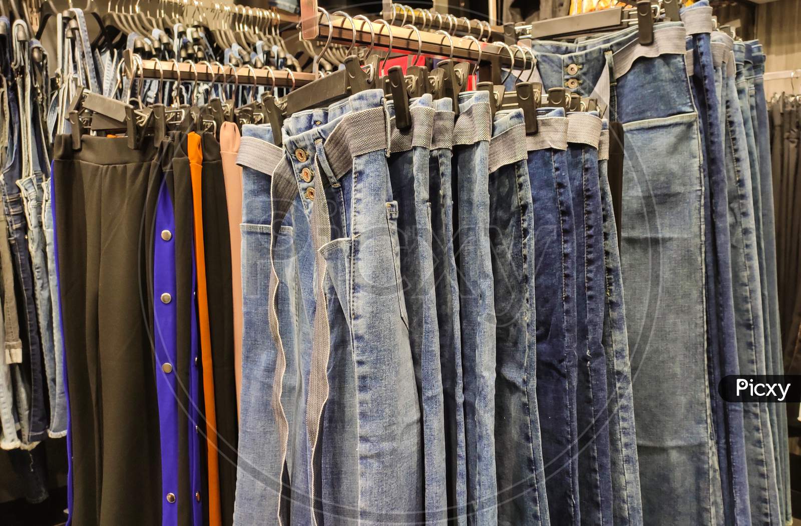 Blue Denim Made Of Jeans Hanging On Hangers In A Row Inside A Clothing Store Ready To Be Sold. Making An Abstract Pattern.