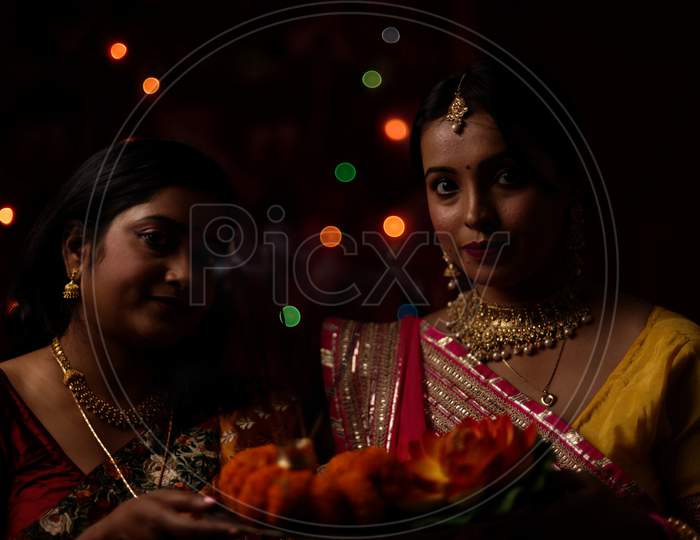 Two beautiful Indian Bengali women in Indian traditional dress celebrating Diwali with incense sticks and flowers in light bokeh background on Diwali evening. Indian lifestyle and Diwali celebration