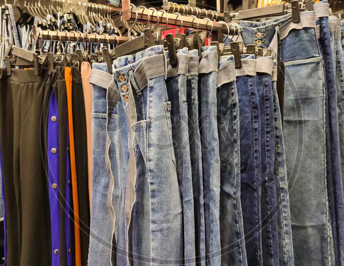 Blue Denim Made Of Jeans Hanging On Hangers In A Row Inside A Clothing Store Ready To Be Sold. Making An Abstract Pattern.