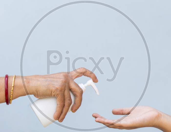 Close Up Of Child And Senior Woman Hand Using Hand Sanitizer Against Plain Background