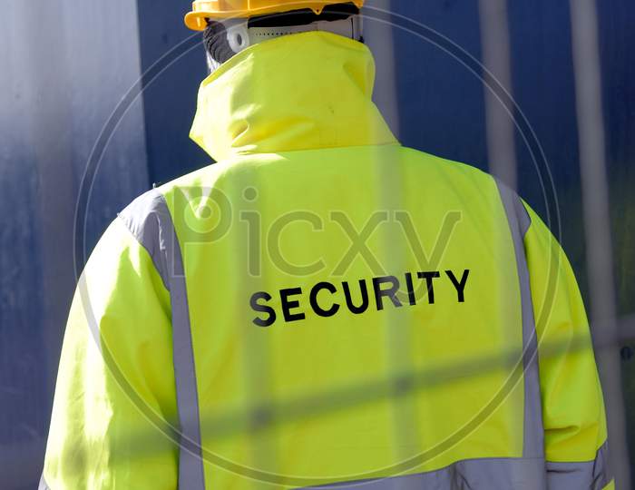 Security Worker Behind Metal Fencing Protecting Property.