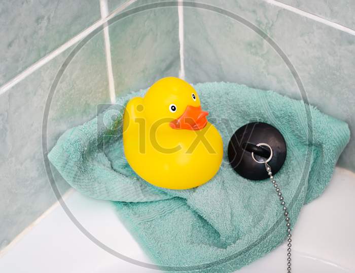 Yellow rubber duck in the bathroom with a towel and bath plug