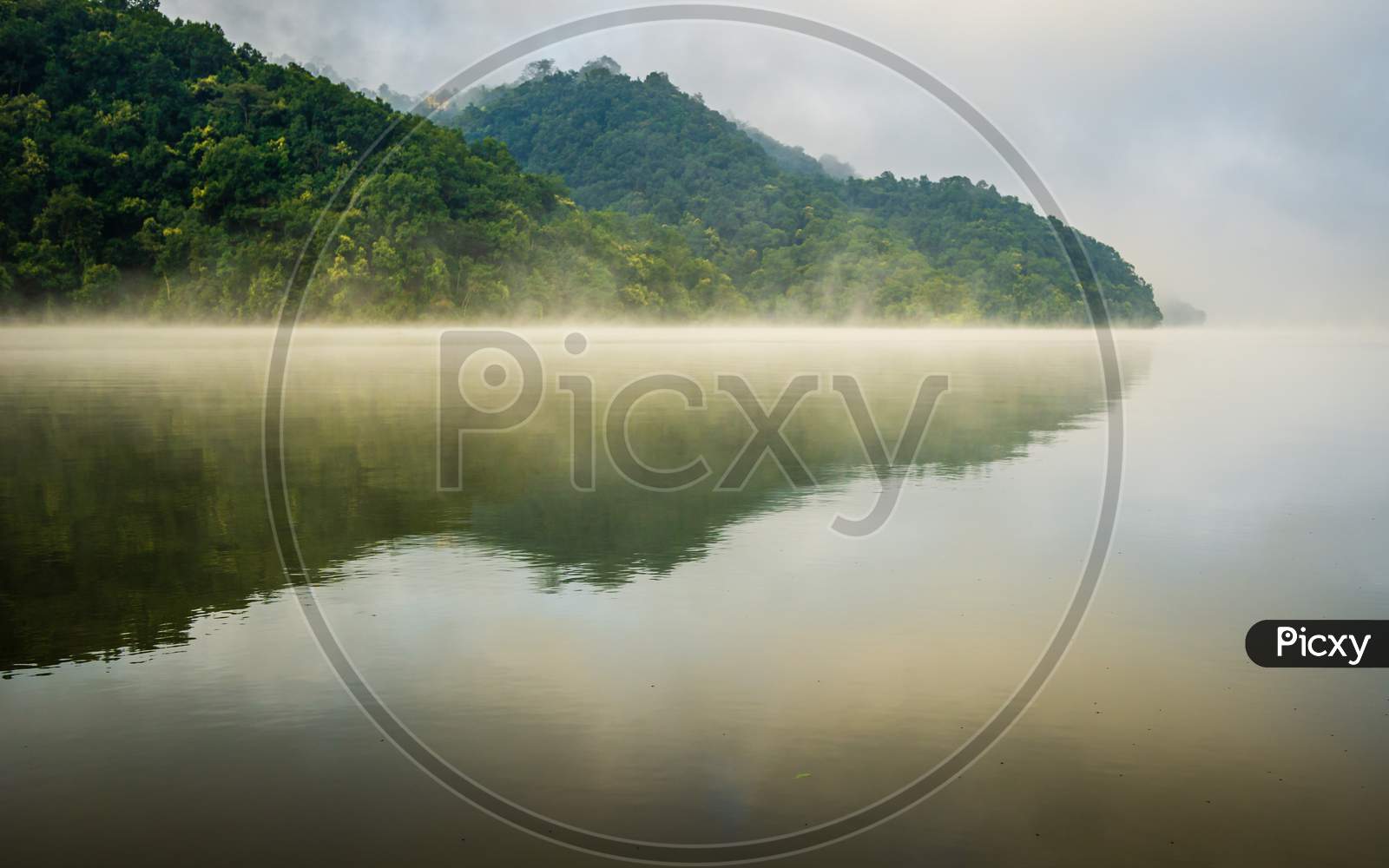 Reflections of hills and forests on foggy surface of Begnas Lake in Pokhara, Nepal