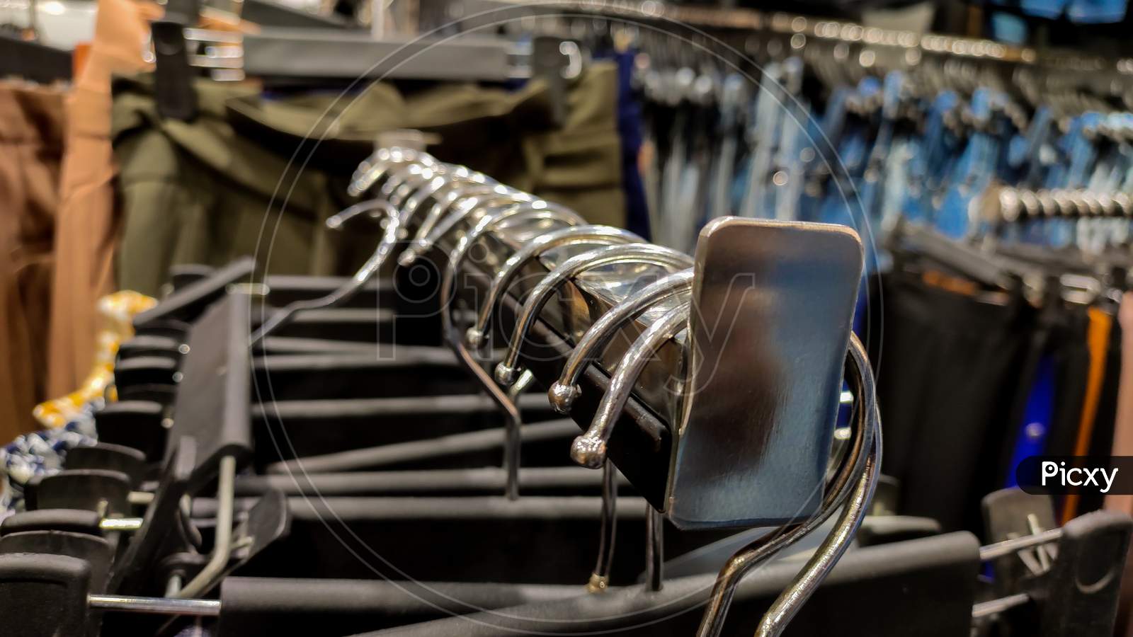 Metallic Hangers hanging on a rod in a clothing store with clothes in it.