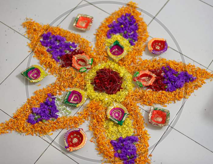 Beautiful holy rangoli is prepared by vibrant colorful flowers and decorative colorful diyas/lamps in white floor. Indian lifestyle and Diwali celebration.