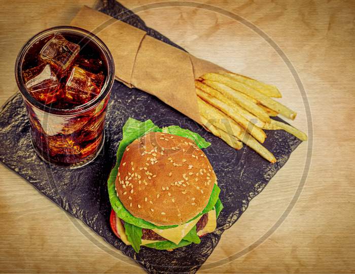 Burger, fries and iced drink on wooden plate
