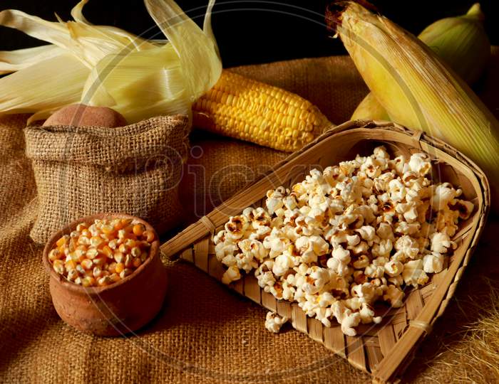 Bowl with tasty traditional popcorn and corncobs on grey wooden background