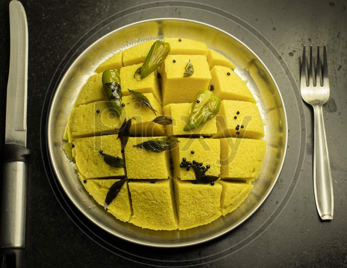 Slices Of Besan Dhokla An Indian Gujrati Vegetarian Food On Plate With Fork And Knife On Black Background