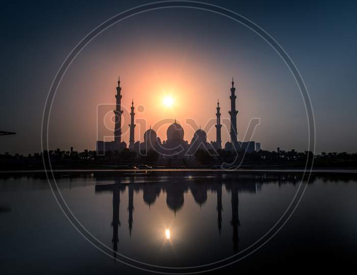 The Sheikh Zayed Grand Mosque with reflection on water and a beautiful golden hour sunset view
