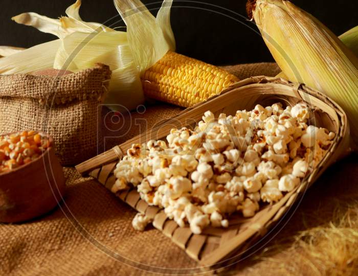 Bowl with tasty traditional popcorn and corncobs on grey wooden background