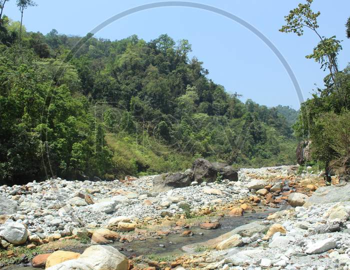 Dry River And A Narrow Flowing Water In The Background Of Blue Sky And Green Mountain