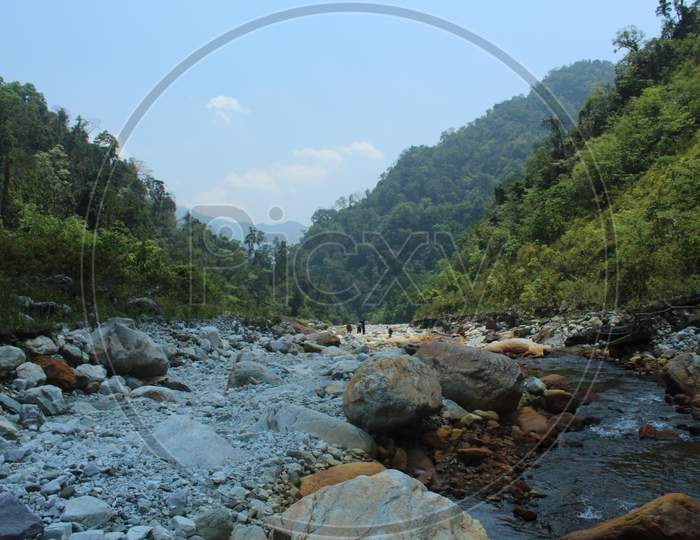 Dry River And A Narrow Flowing Water In The Background Of Blue Sky And Green Mountain