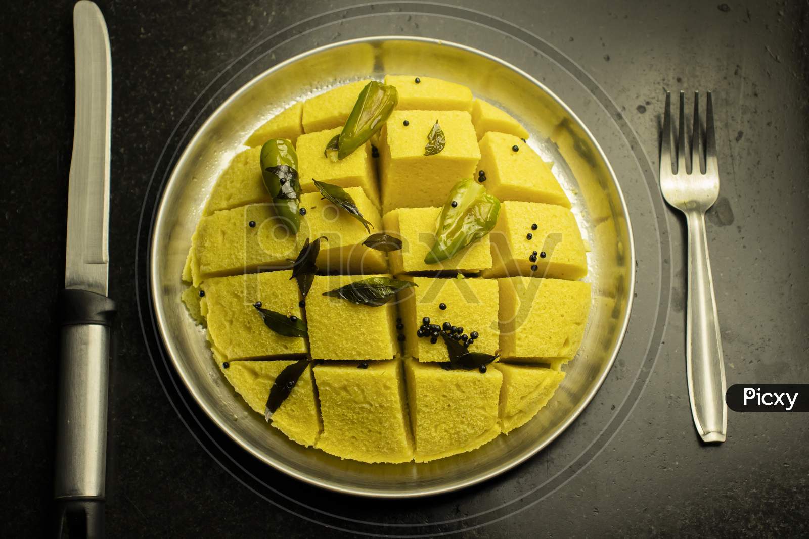 Slices Of Besan Dhokla An Indian Gujrati Vegetarian Food On Plate With Fork And Knife On Black Background