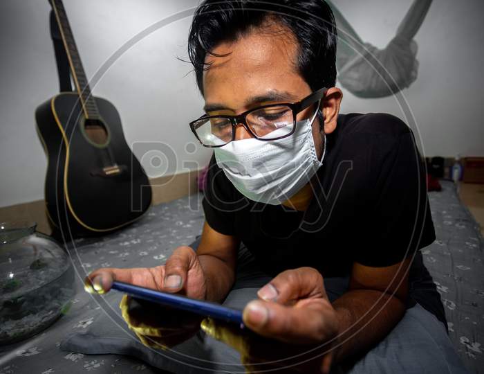 A Surgical Mask-Wearing Young Man Was Playing Mobile Games On His Own Home Due To Coronavirus Home-Quarantine At Dhaka.