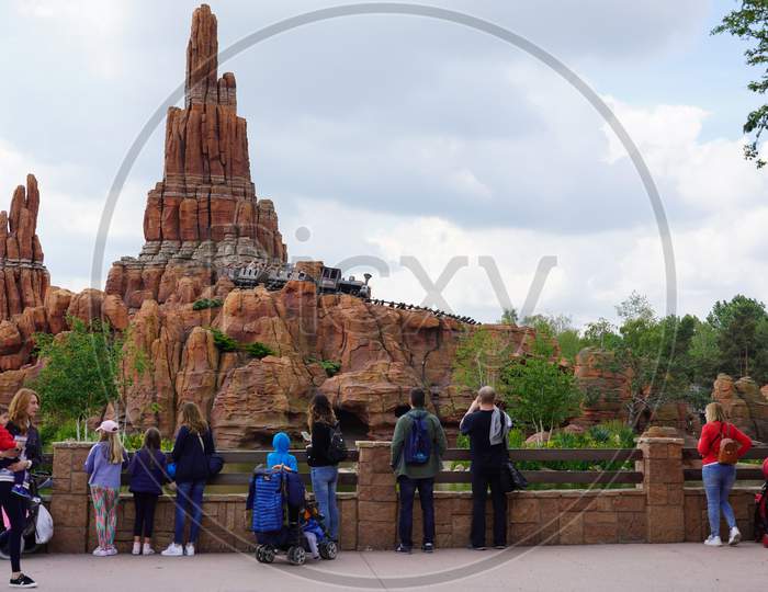Standing with other visitors on a street of a theme park wild west in front of an high rock in France. Steam locomotive transporting passengers on bright day with cloudy sky. Paris France, 29. May 2019.