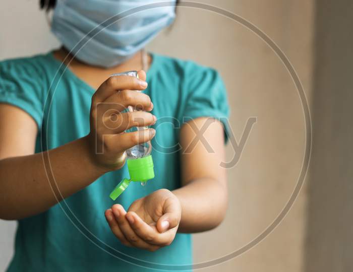 An Indian Asian Girl Child Wearing Safety Nose Mask Sanitizing Hands During Novel Corona Virus Or Covid-19 Outbreak With Selective Focus, Shallow Depth Of Field And Blurred Background