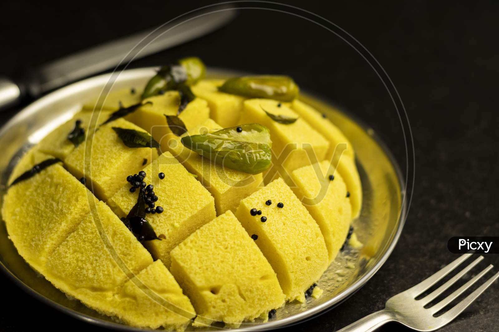 Slices Of Besan Dhokla An Indian Gujrati Vegetarian Food On Plate With Fork And Knife On Black Background And With Selective Focus